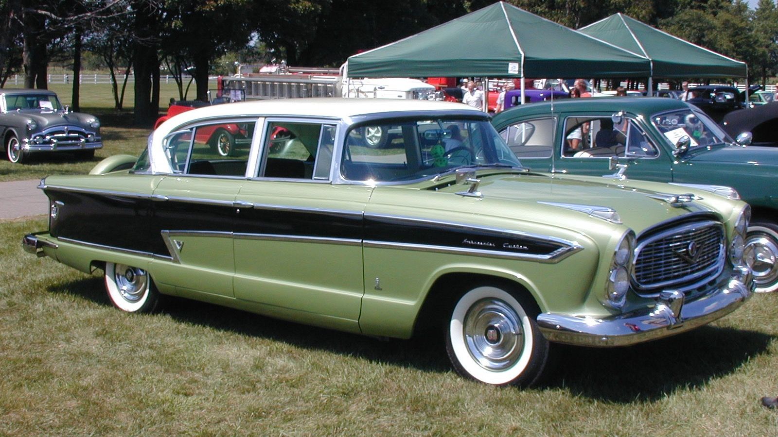 Green and black 1957 Nash Ambassador Custom four-door sedan, front three-quarter view on grass at an outdoor car show