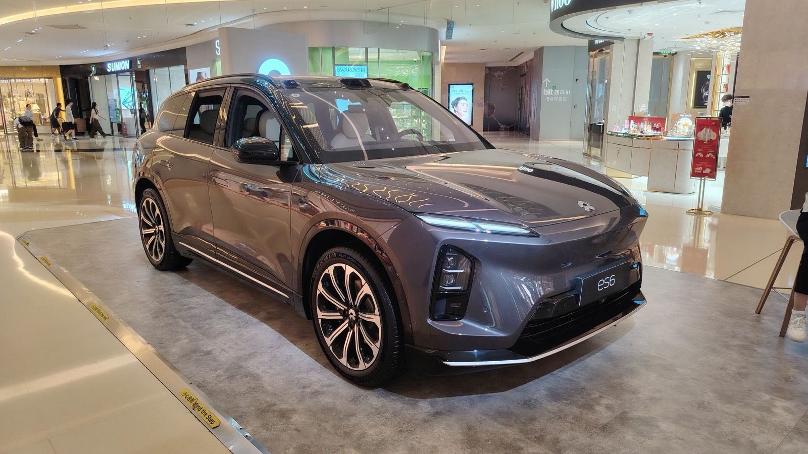 Dark grey 2025 NIO ES6 displayed in a shopping mall, front three-quarter view