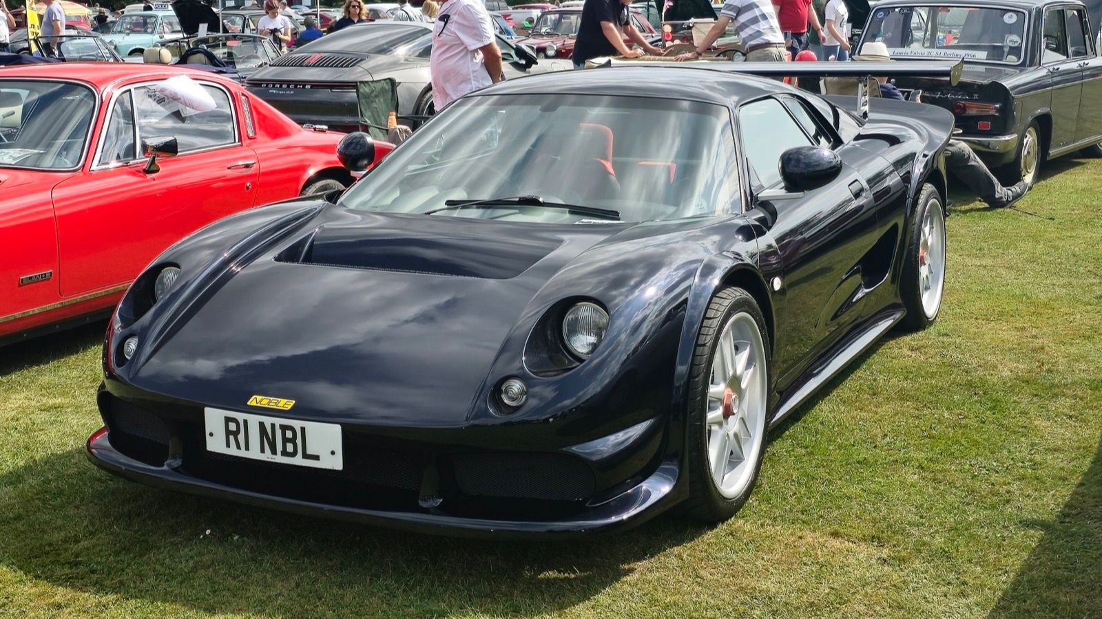 Dark blue 2001 Noble M12 GTO parked on grass at a car show, front three-quarter view