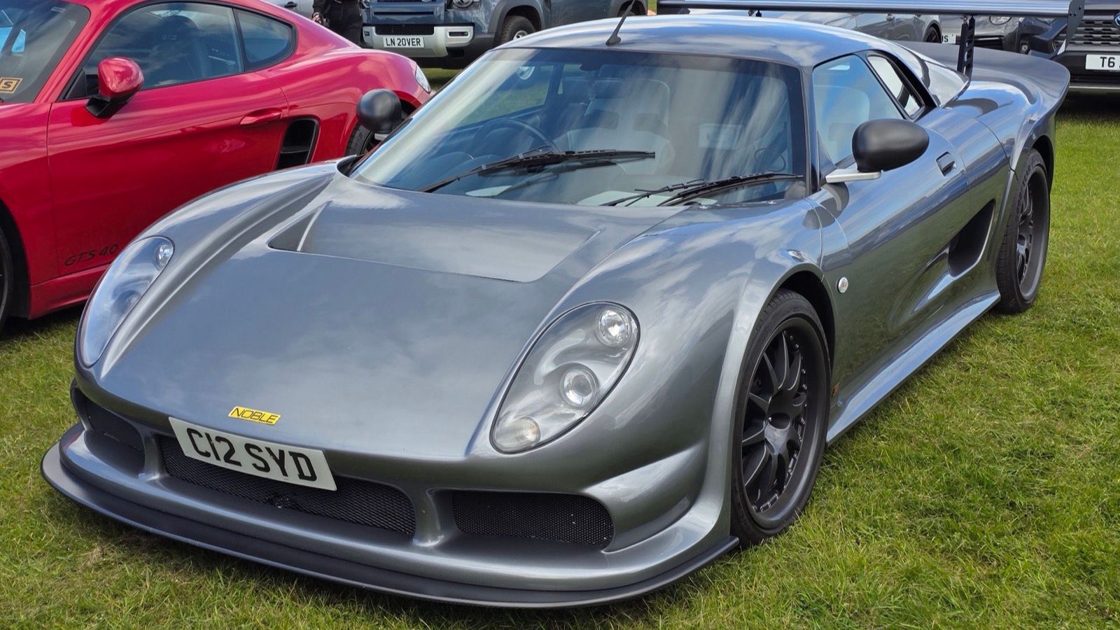 Grey 2004 Noble M12 GTO-3R with black wheels parked on grass, front three-quarter view