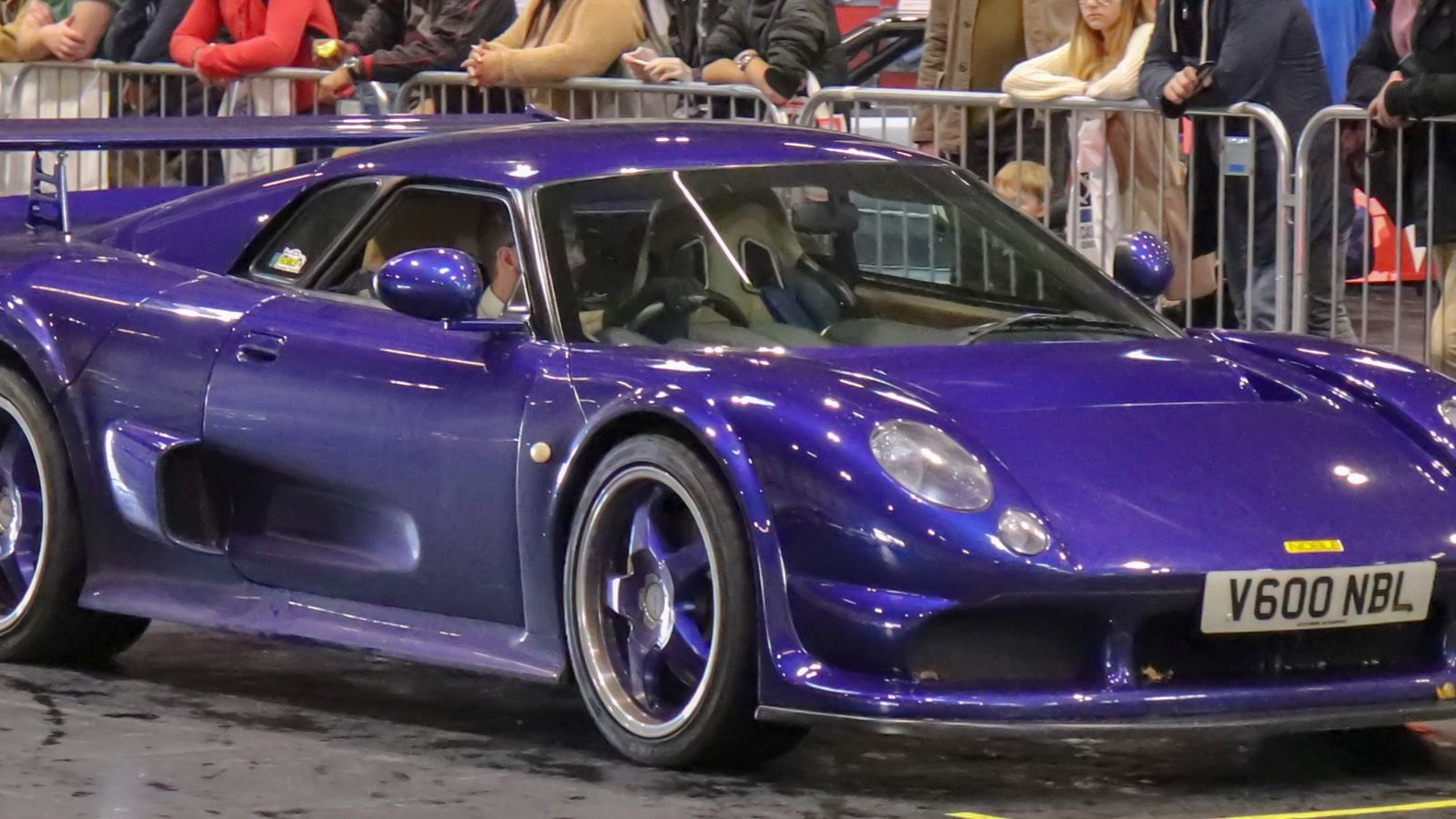 Purple Noble M12 GTO 2.5 coupe with rear wing on an indoor show floor, front three-quarter view