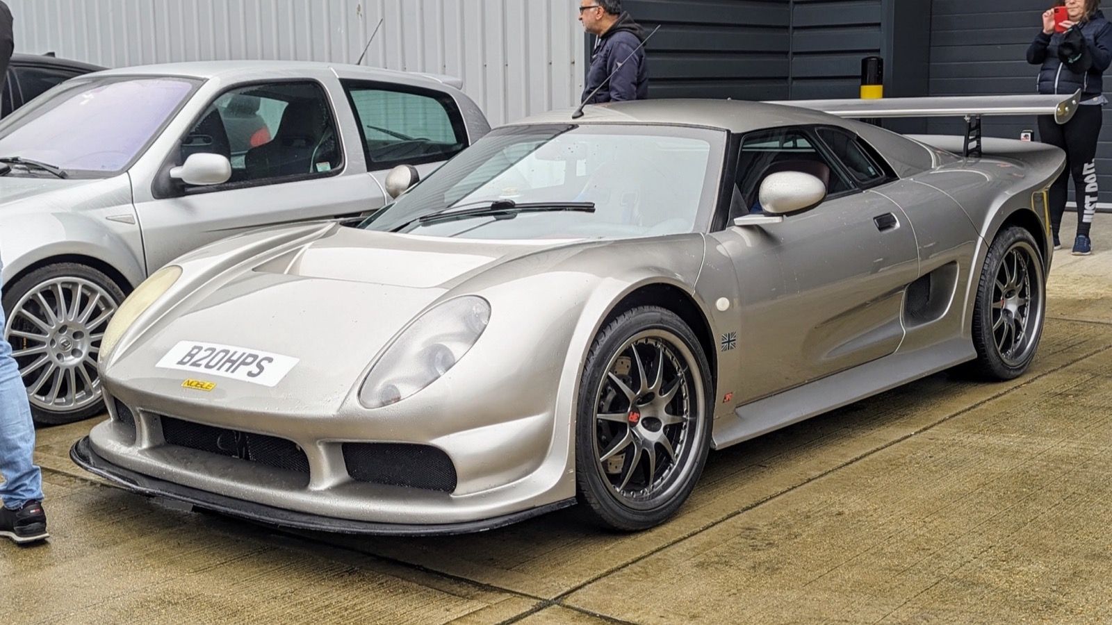Silver Noble M12 GTO-3R with tall rear wing on a workshop forecourt, front three-quarter view