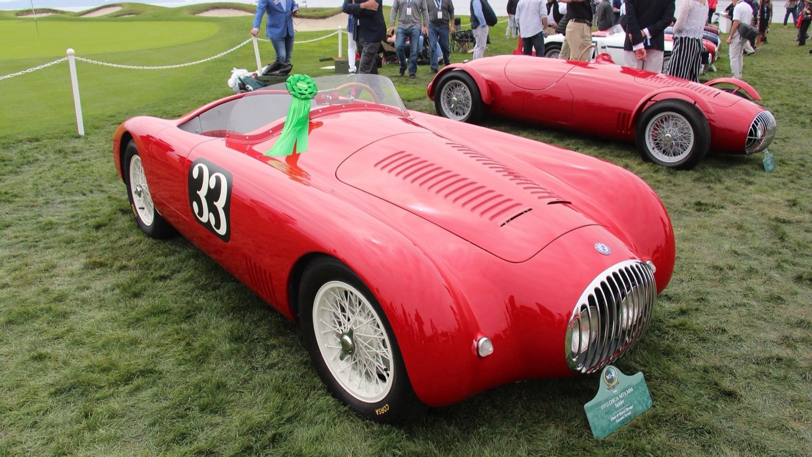 Red 1952 OSCA MT4 MM spyder racing number 33 on a concours lawn, rear three-quarter view