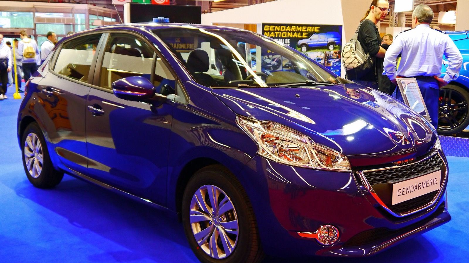 Blue first-generation Peugeot 208 five-door hatchback on a motor-show stand, front three-quarter view