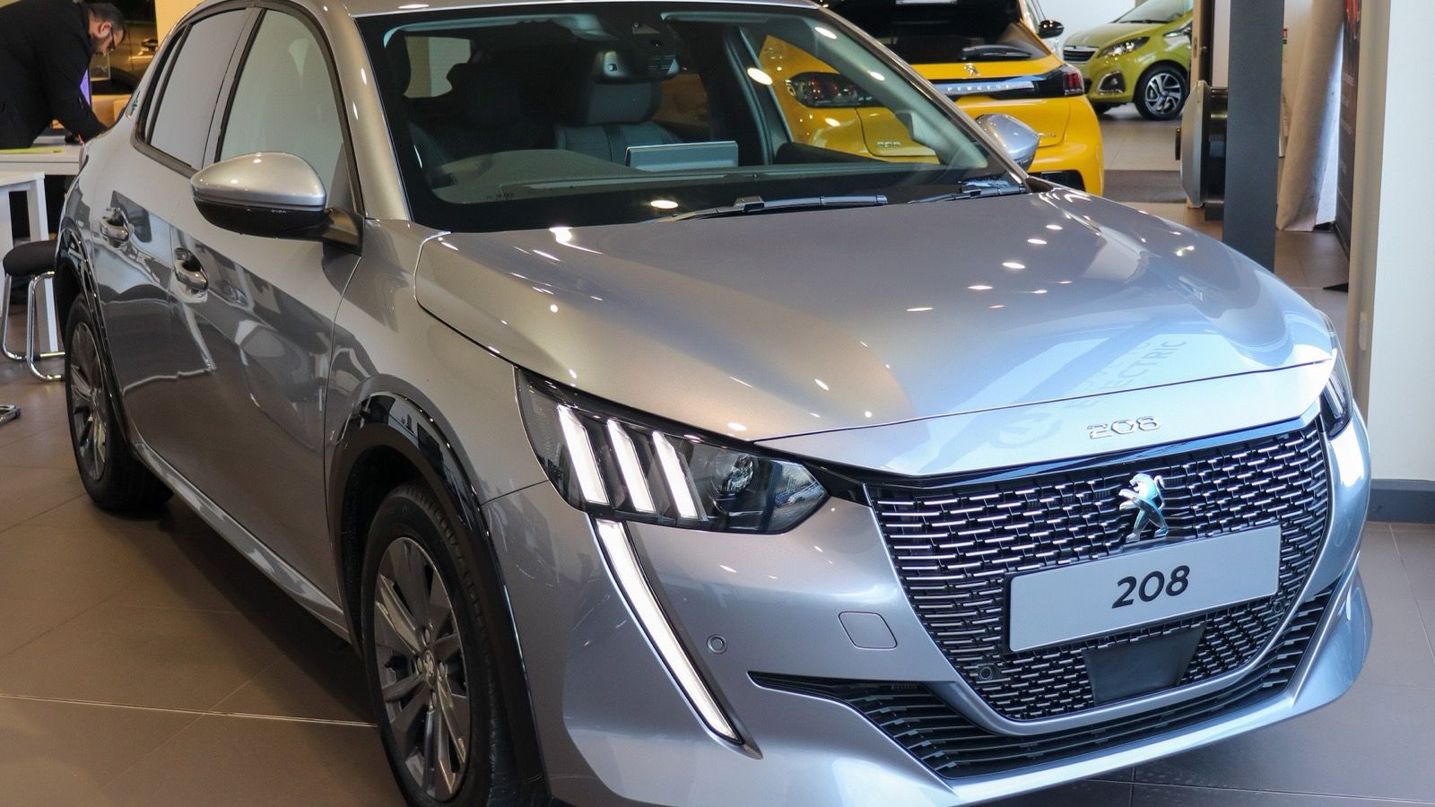 Silver 2020 Peugeot e-208 Allure electric hatchback in a showroom, front three-quarter view