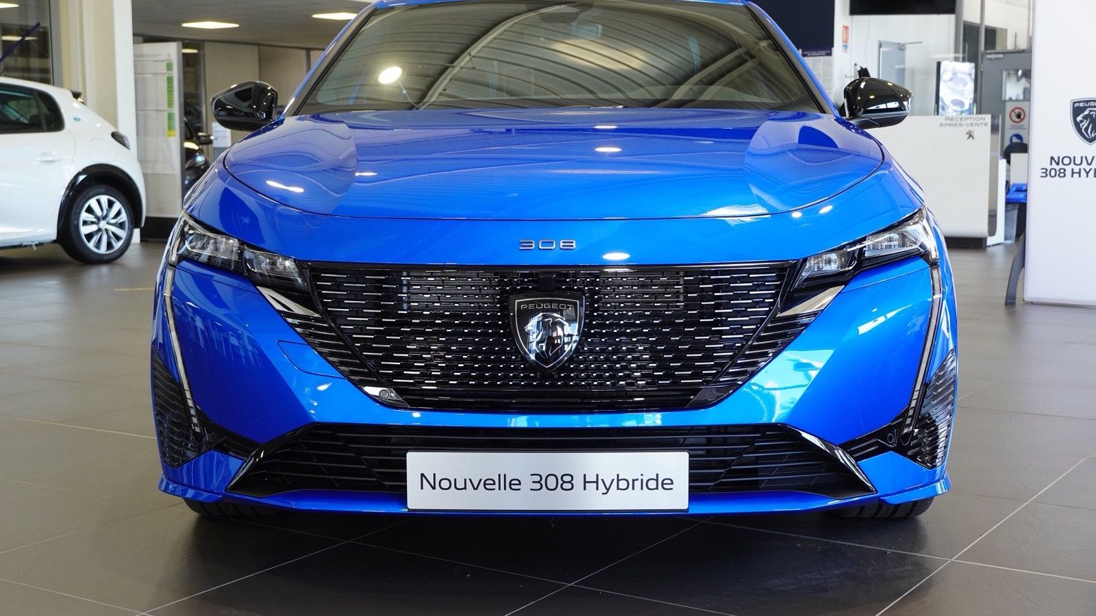 Blue third-generation Peugeot 308 Hybrid in a dealership, front view showing the fang-style running lights