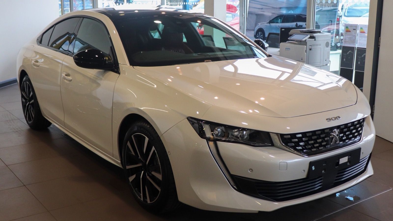 White 2020 Peugeot 508 GT Hybrid fastback in a showroom, front three-quarter view