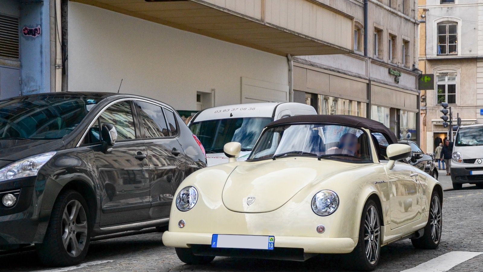 Cream PGO Speedster II roadster with raised soft top parked on a city street, front three-quarter view