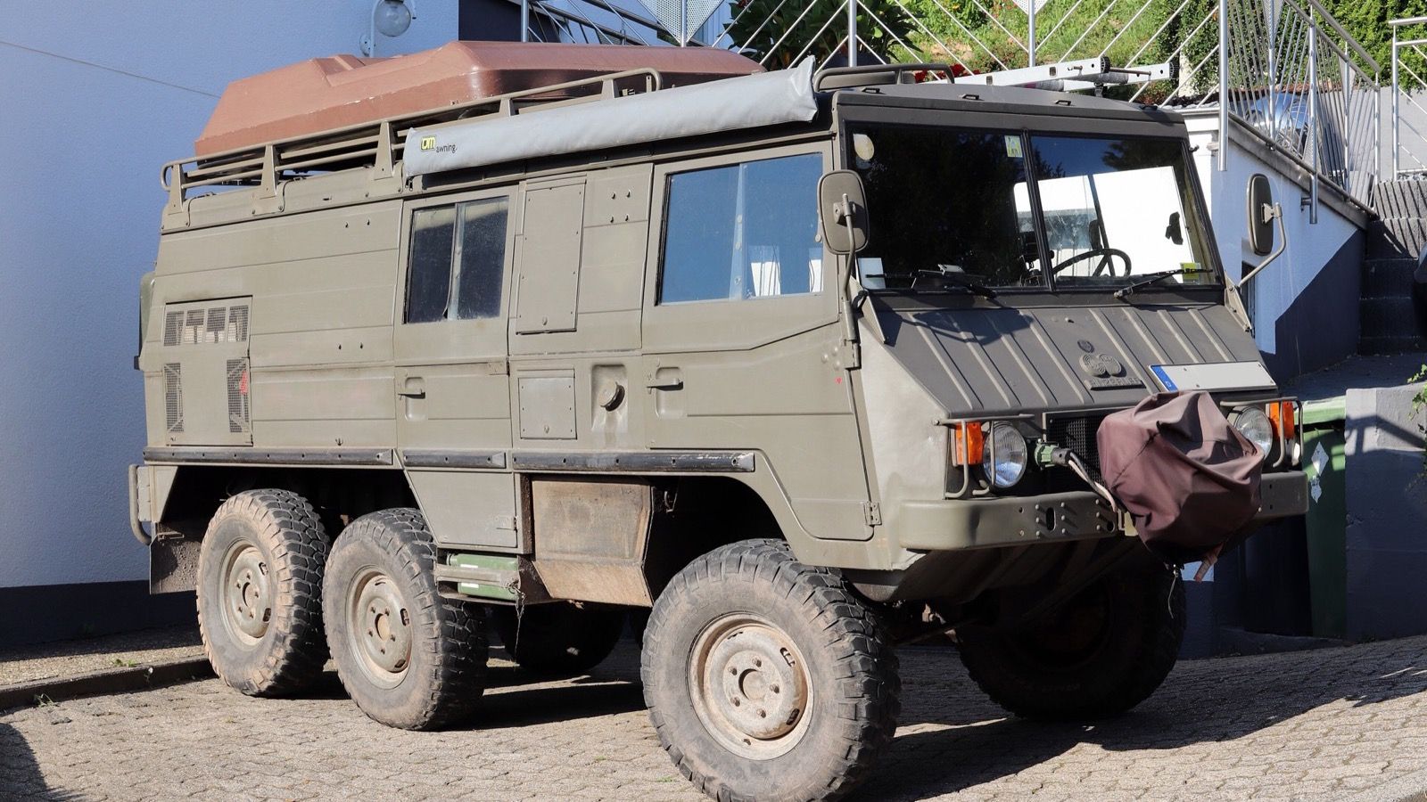 Olive green Steyr-Puch Pinzgauer 6×6 parked on cobbles, front three-quarter view