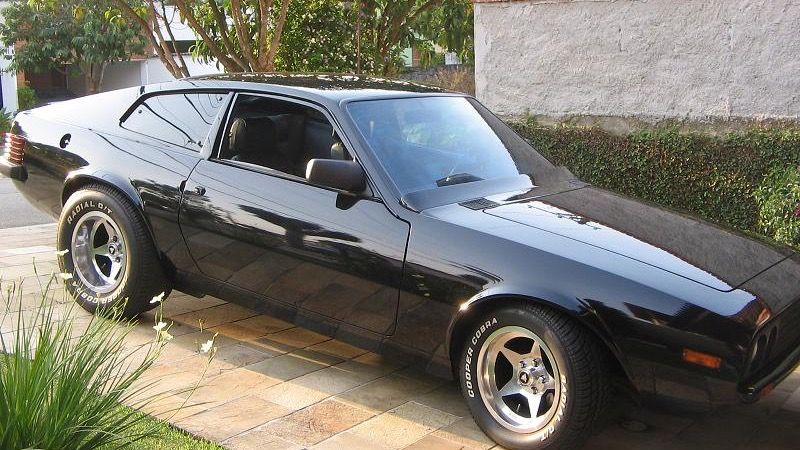 Black 1980 Puma GTB S2 coupe on a paved driveway, front three-quarter view showing the long fastback profile