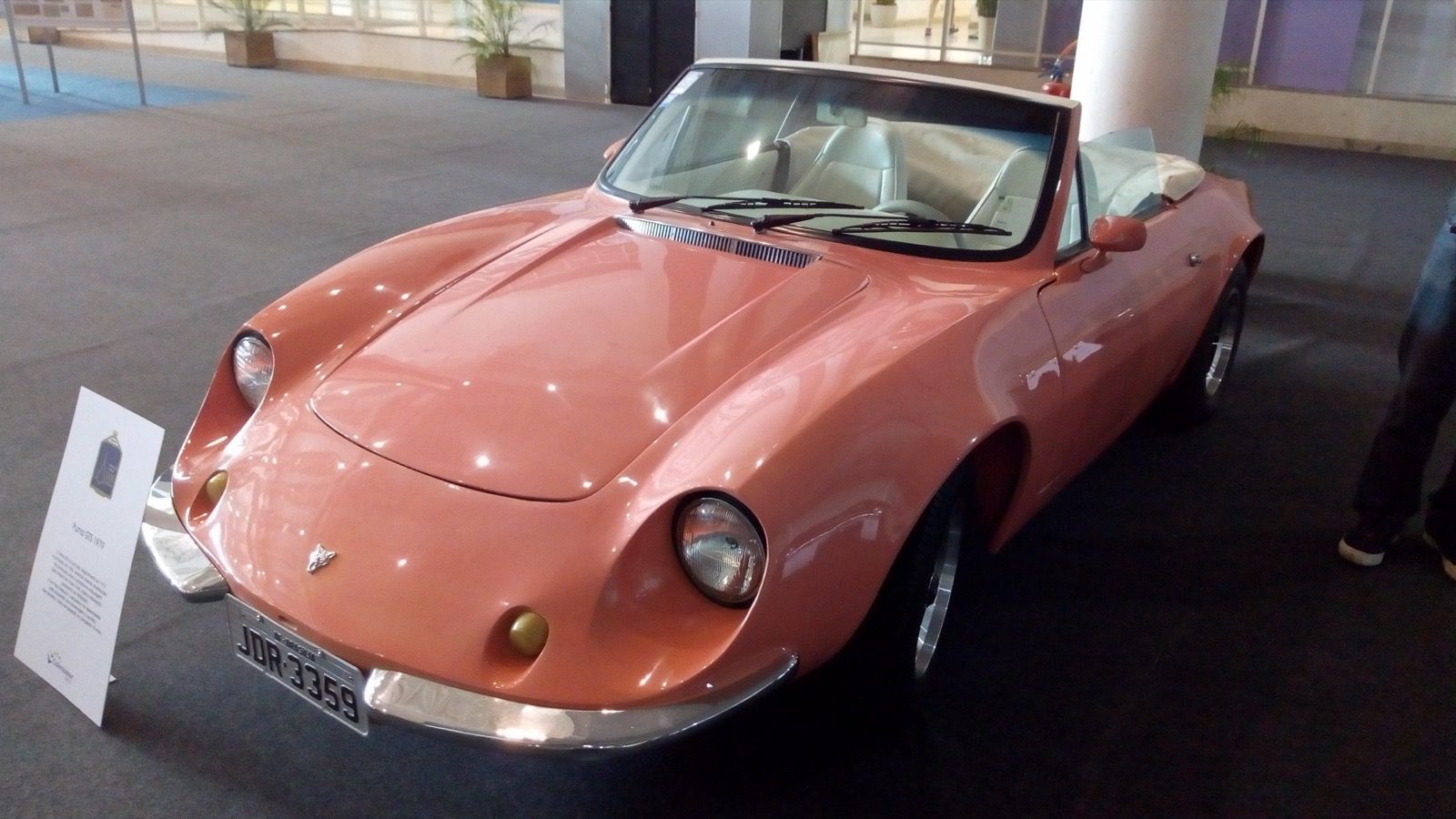 Salmon-coloured 1979 Puma GTS roadster with the top down, front three-quarter view on indoor display