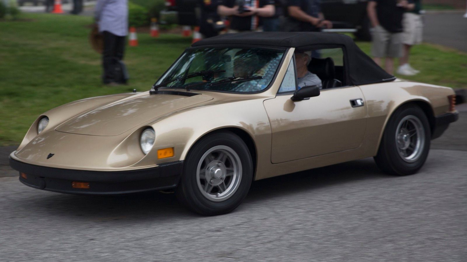 Gold 1983 Puma GTC roadster with black soft top raised, front three-quarter view being driven at a Greenwich concours