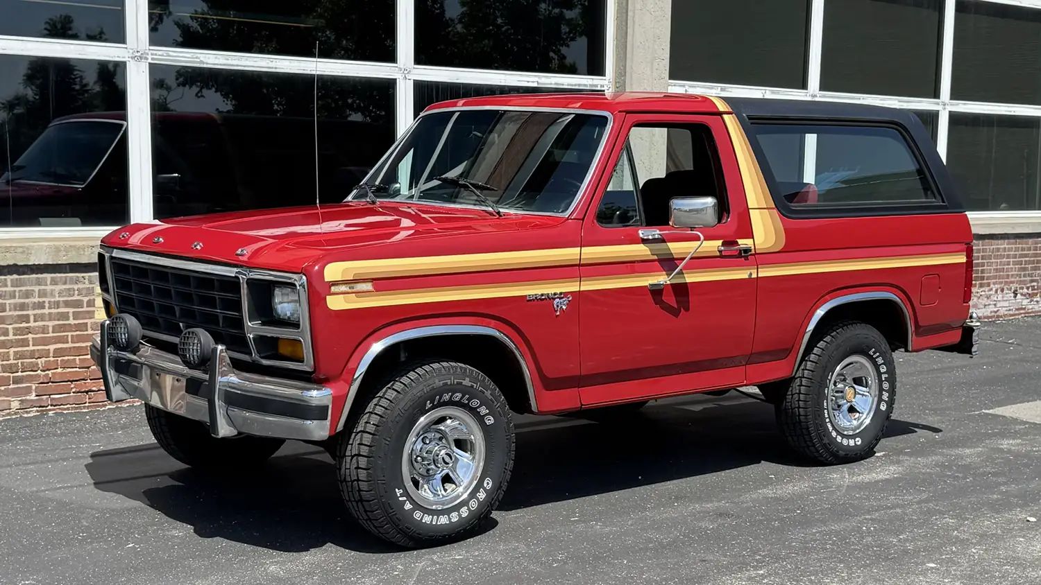 1981 Ford Bronco, red full-size SUV with stripes and large wheels, front three-quarter view