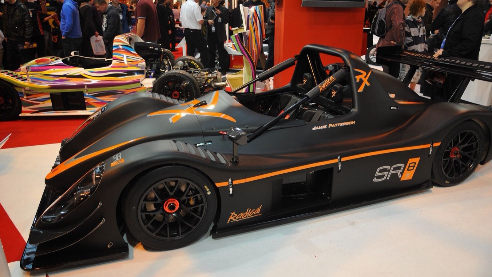 Matte black Radical SR8 RX with orange graphics displayed at Autosport International 2011, side profile