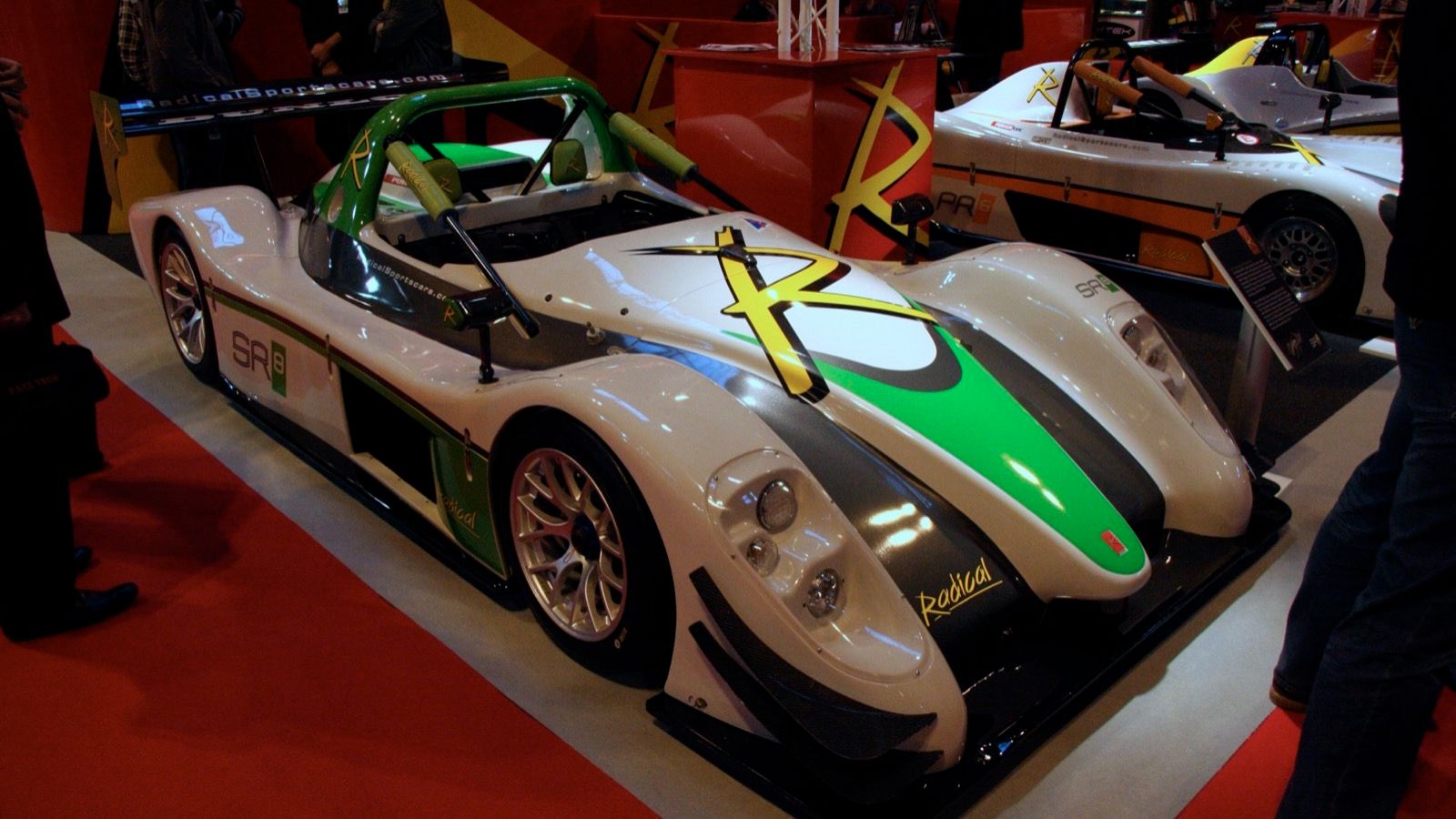 White and green first-generation Radical SR8 open sports prototype on a motor show stand, front three-quarter view