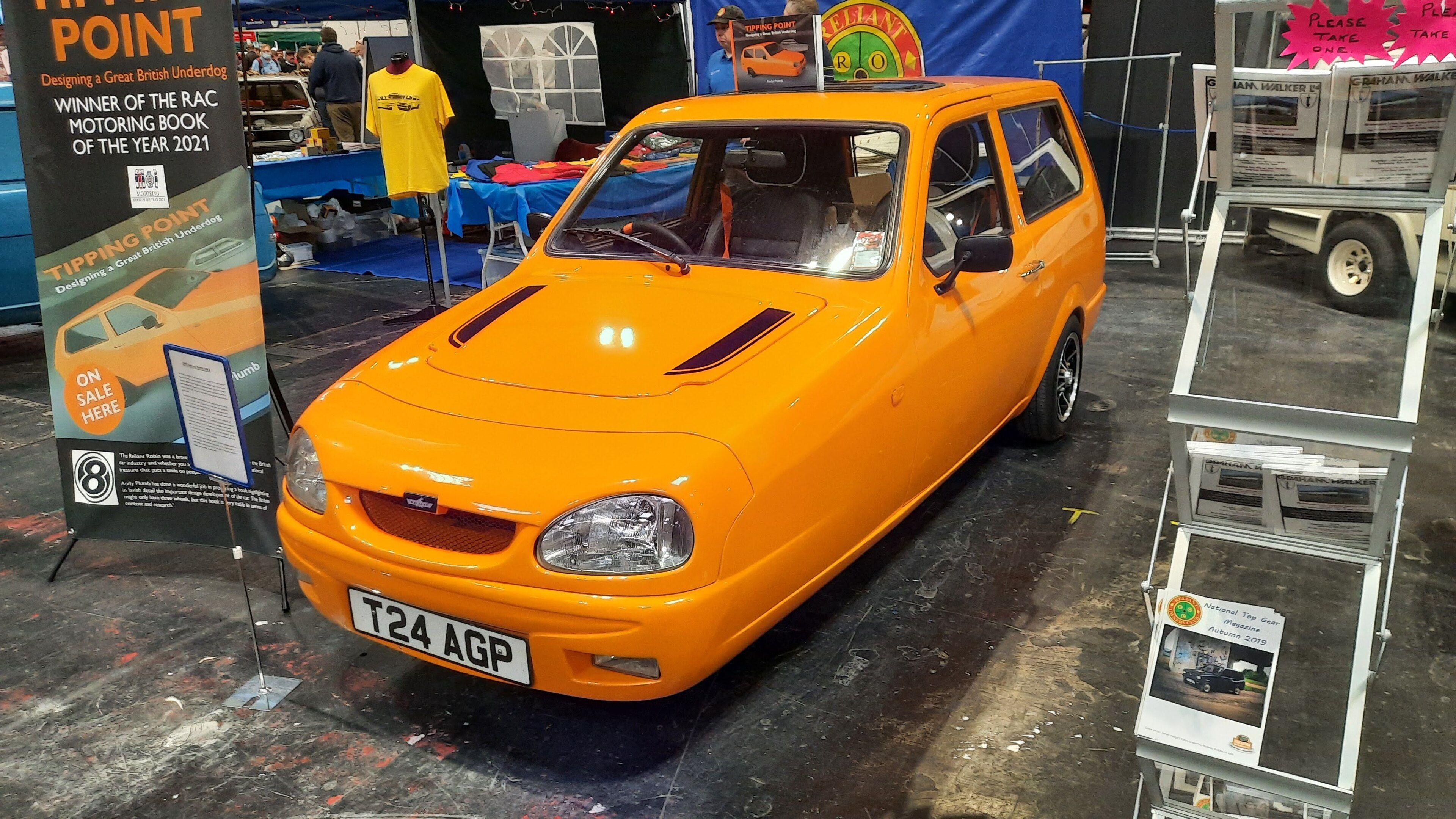 Orange 2000 Reliant Robin 848cc SLX on indoor show display, front three-quarter view