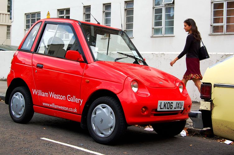 Red 2006 REVA G-Wiz in London livery, front three-quarter view