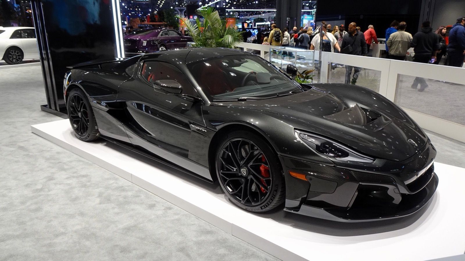 Black Rimac Nevera hypercar on an auto-show stand, front three-quarter view