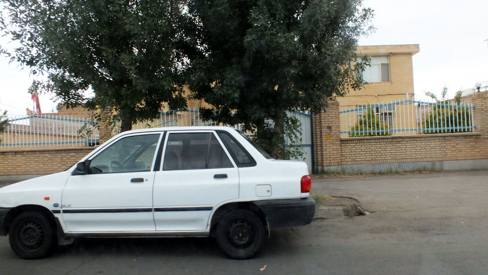 White SAIPA-built Kia Pride four-door sedan parked on a street in Kashmar, Iran, side profile