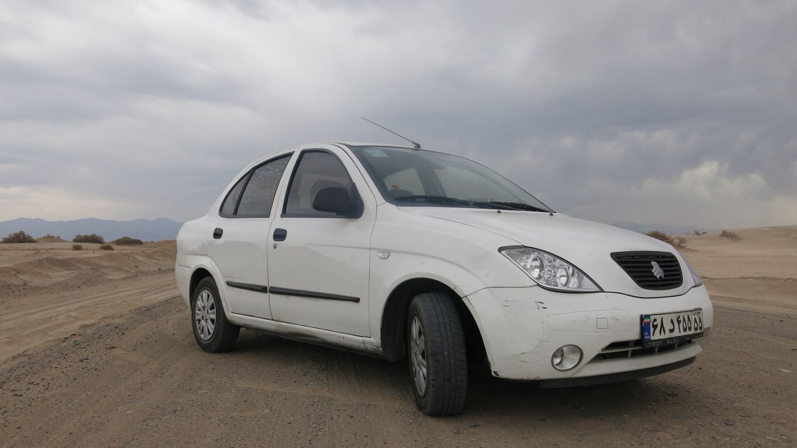 White SAIPA Tiba four-door sedan on a desert track in Iran, front three-quarter view