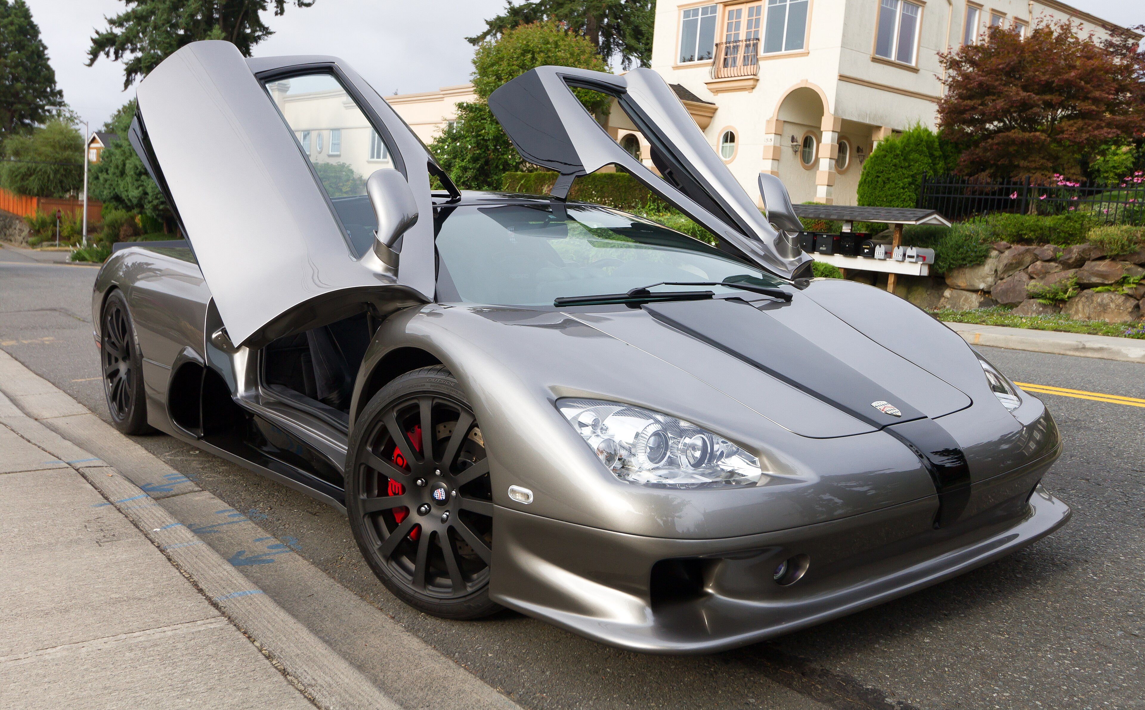 Grey SSC Ultimate Aero TT with scissor doors raised, front three-quarter view on a residential street