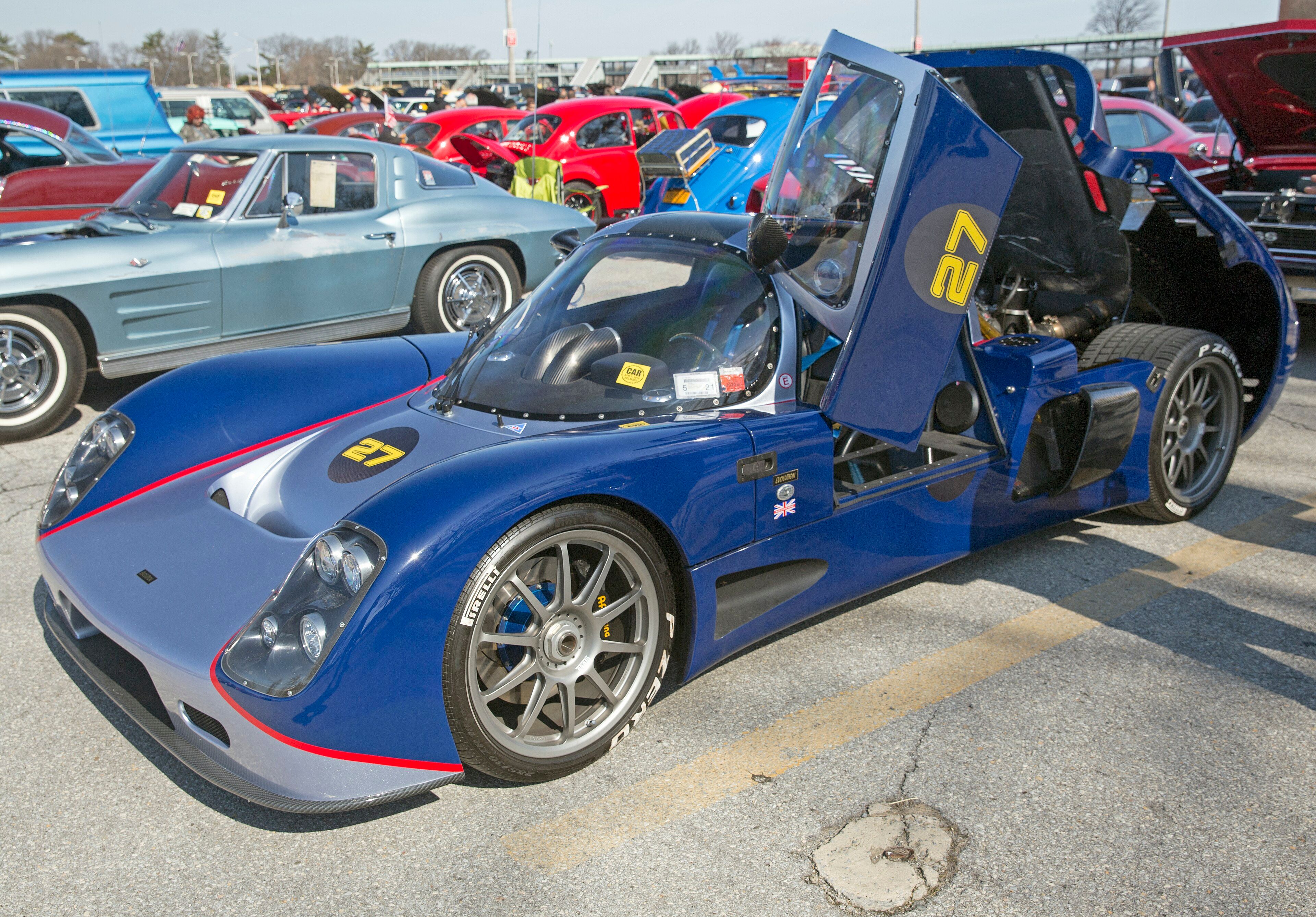 Blue Ultima Evolution coupe with butterfly door raised, front three-quarter view